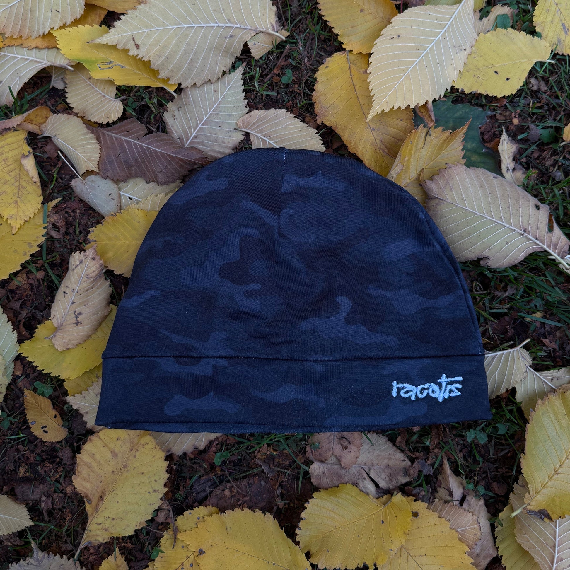 Blue camouflage beanie with 'roots' branding on a bed of autumn leaves.