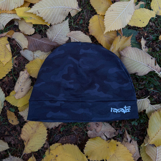 Blue camouflage beanie with 'roots' branding on a bed of autumn leaves.